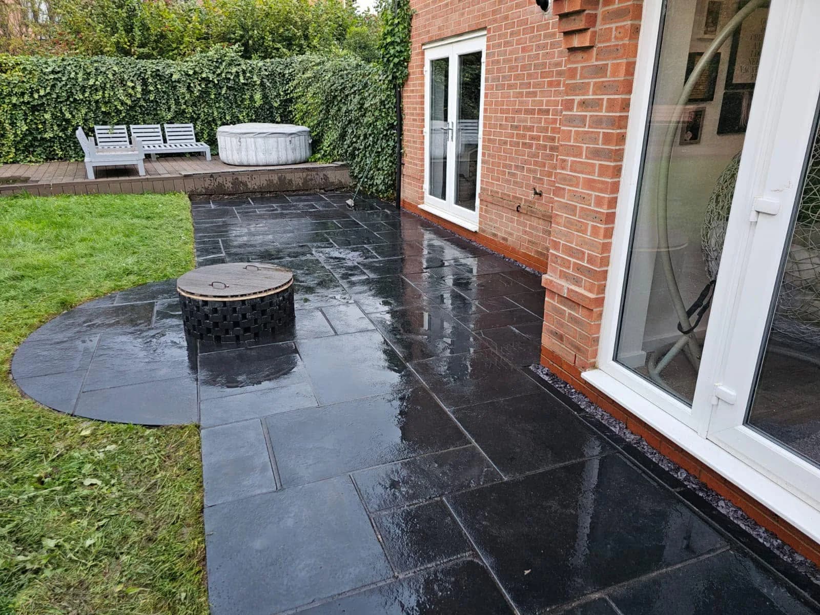 Dark natural stone patio with a circular feature beside a green lawn