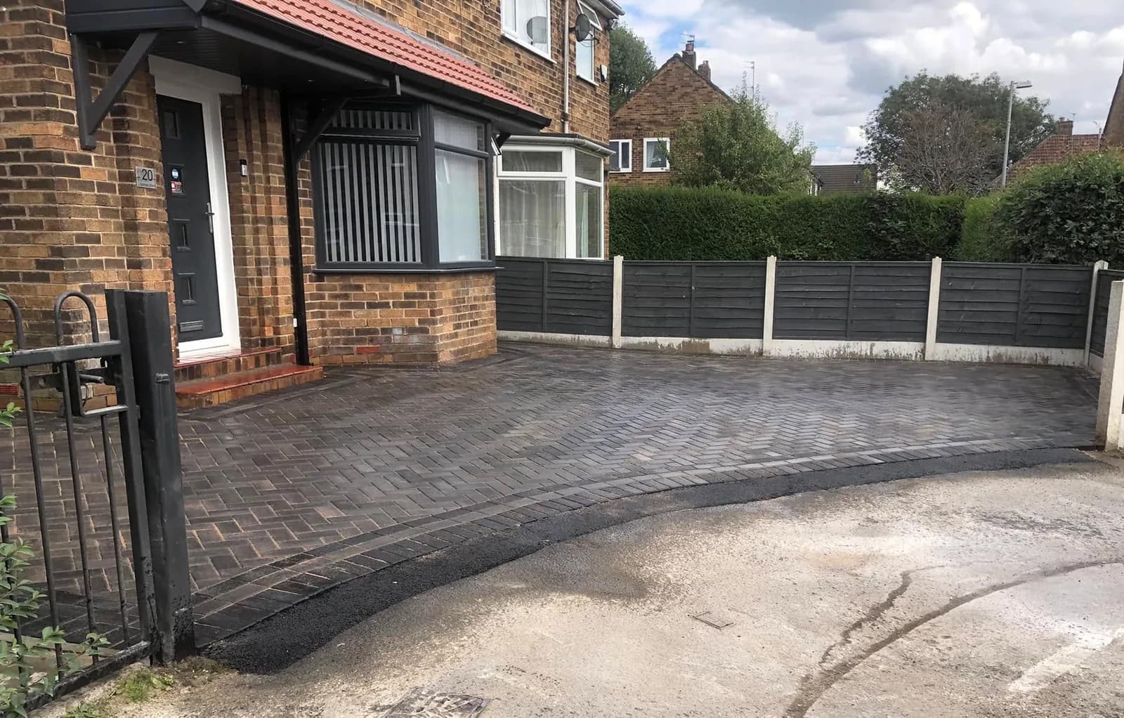 Completed charcoal block-paved driveway behind an open garden gate